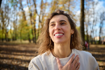 Portrait of a young smiling woman in an autumn park on a bright sunny day. Close-up view. Fall time.