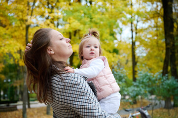 Mother and cute baby girl walking in autumn park with leaves on the ground. Mom spending time with a small child in the park. ?oncept of a good mother-child relationship.