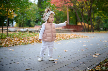 Fototapeta premium Small pretty girl walking in the park full of colorful leaves on the ground. Cute baby girl in the park. Child carrying leaves in the park