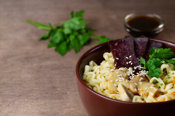 Japanese ramen noodles with chicken, boiled egg, mushrooms, spring onions and soy sauce. Korean soup. Traditional Asian cuisine. A brown bowl of Korean soup with food sticks on the dark. copy space