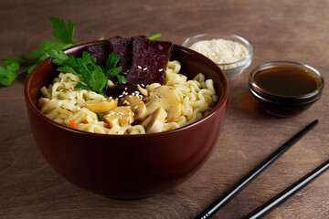 Japanese ramen noodles with chicken, boiled egg, mushrooms, spring onions and soy sauce. Korean soup. Traditional Asian cuisine. A brown bowl of Korean soup with food sticks on the dark.