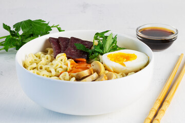 Japanese ramen noodles with chicken, boiled egg, mushrooms, spring onions and soy sauce. A bowl of Korean soup with food sticks. Asian noodle soup in white bowl on the white background. Copy space.