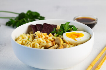 Close-up of Japanese ramen noodles with chicken, boiled egg, mushrooms, spring onions and soy sauce. A bowl of Korean soup with food sticks. Asian noodle soup in white bowl on the white background.