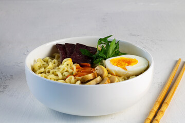 A bowl of Korean soup with food sticks. Asian noodle soup with mushrooms and green onions, ramen with meat, vegetables and eggs in white bowl on the white background. Copy space.