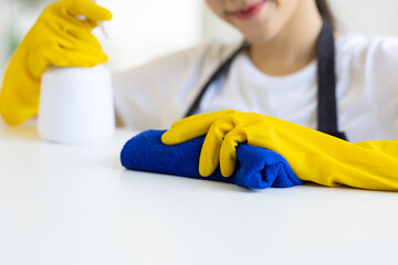 A young woman wearing an apron is cleaning a table in her home office using disinfectant and a wipe.