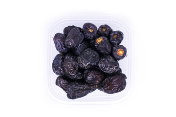 Close-up view of a large pile of delicious Ajwa dates in a transparent food container to keep food hygienic isolated on white background. Arabic healthy food concept.