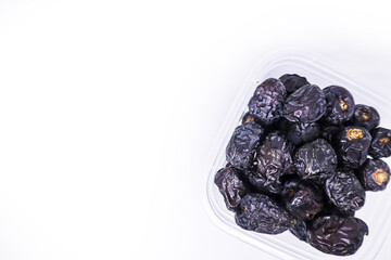 A pile of large delicious Ajwa dates in a transparent food container to keep food hygienic isolated on white background. Arabic healthy food concept. Top view with copy space.