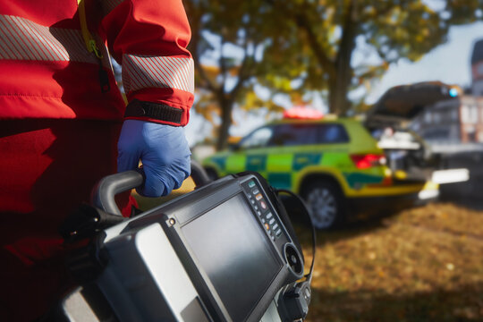 Emergency medical service. Close-up of paramedic hand in blue surgical gloves while running with defibrillator monitor against ambulance car. Themes rescue, urgency and health care.