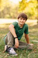 Vertical photo of teenager boy sitting on grass in park after school and relaxing.