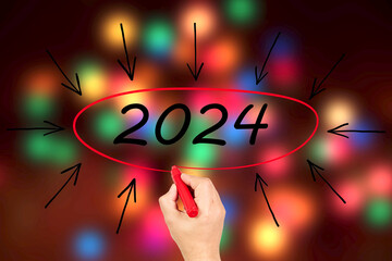 2024, Woman writing the number 2024 on background of faded lights. Happy New Year