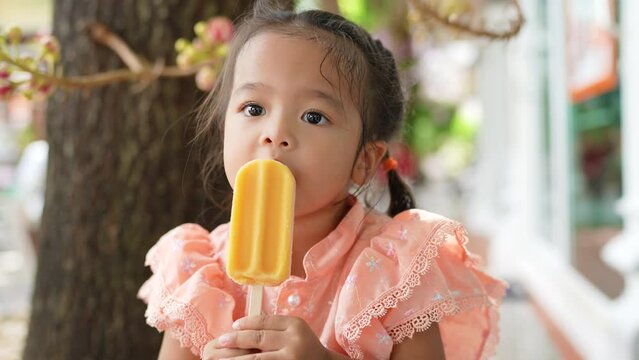 Little asian Thai girl enjoying eat ice cream wear raditional Thai suit in buddhist temple outdoor summer vacation