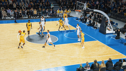 Basketball Championship in a Crowded Arena: Yellow Team Passing the Ball, Player Aiming To Score a...