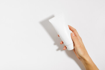Female hand holding white mockup tube of face or body cream on white isolated background. The...