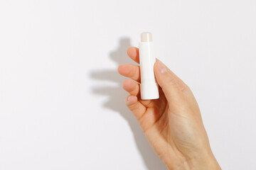 Female hand holding clear protective lip balm on white isolated background. Mockup for your design. The concept of decorative cosmetics for health and beauty