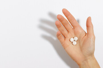 Close-up of a female hand holding three pills or vitamins on a white isolated background. Concept...