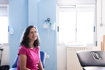 A middle aged woman with brunette hair sits on the hospital bed and waiting to start rehabilitation.
