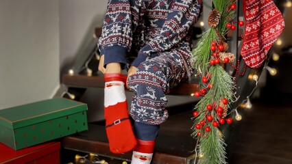 Closeup of little boy in pajamas putting on warm funny Christmas socks