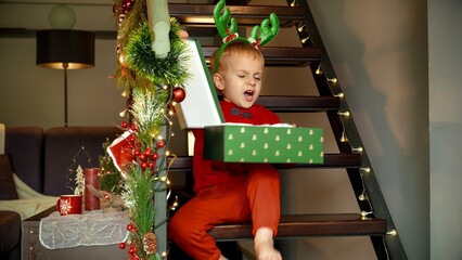Upset and angry toddler boy opens his Christmas gift and gets disappointed throwing down the...