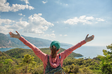 Beautiful traveler woman with hands up on mountain peak looking at the sea water in summer