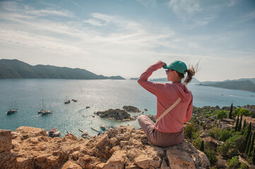Beautiful traveler woman sitting on mountain peak looking at the sea water in summer