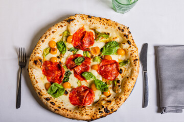 Pizza tradizionale napoletana con salame piccante, mozzarella, basilico e pomodorini gialli servita in una pizzeria - obrazy, fototapety, plakaty