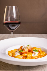 Piatto di gnocchi con pomodori, burrata pugliese, basilico e formaggio grattugiato accompagnato da un calice di vino rosso e servito come primo piatto in un ristorante