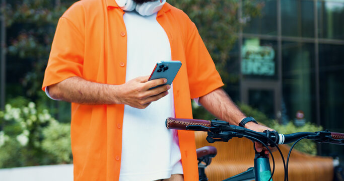 Close-up. Man using phone to rent and ride a bike commuting in the city. Guy is pushing his bike and surfing the Internet. Chatting while cycling. Modern lifestyle connection.
