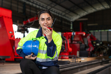 Engineer woman smart female indian worker supervisor with safety suit work in robot metal machinery factory operator radio control.