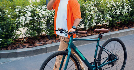 Portrait caucasian man going near business centre carrying the bicycle using smartphone. Hipster guy have call, wearing glasses, walking in the city with bicycle city. Technology and city life.