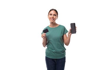 young slender woman dressed in a green basic straight cut t-shirt holds a credit card with a mockup and a smartphone