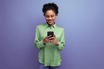 young positive latin woman dressed in a green shirt chatting on a smartphone