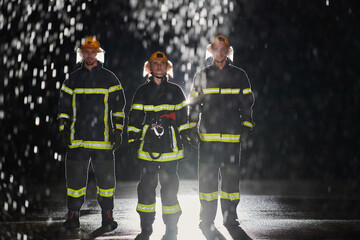 A group of professional firefighters marching through the rainy night on a rescue mission, their...