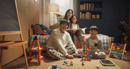 Happy Korean Family Portrait with Adults And Kids Looking at Camera and Smiling in Children's Room. Mother and Daughter Reading Fairy Tale Stories, Father and Son Play with Construction Blocks. - obrazy, fototapety, plakaty