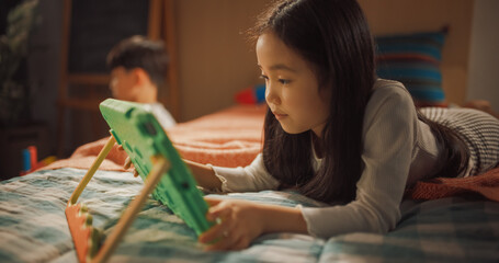 Thoughtful Asian Girl Using a Tablet Computer for Learning at Home in Her Children's Bedroom. Adorable Talented South Korean Child Thinking, Problem Solving a Digital Exercise on a Device