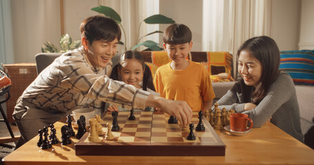 Portrait of a Happy Korean Family Playing Chess in the Living Room. Father and Son Having a Tournament While Mother and Daughter Help. They are Enjoying Spending Quality Time Together