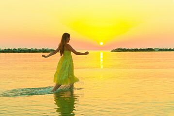 beautiful girl in a yellow dress running on the water at dawn.