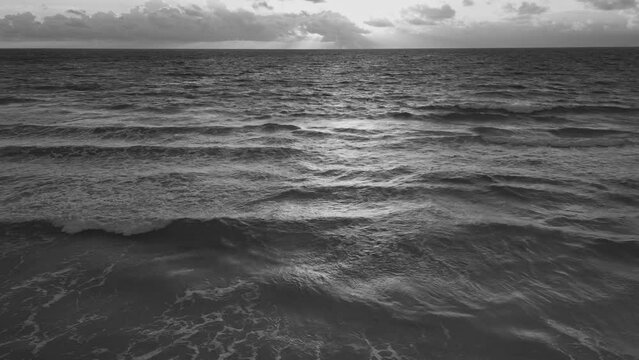 Monochrome shot of the foamy waves of the beach against a clouded sky