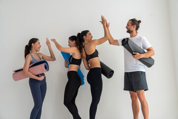 Group of friends and instructor wearing sports bras and yoga clothes, holding yoga mats, finishing yoga class, happy, happy, clapping hands in studio.Health,lifestyle and exercise concept
