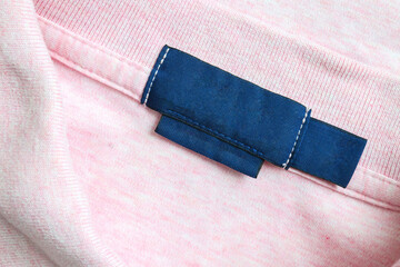 Blank blue laundry care clothes label on pink shirt fabric texture background