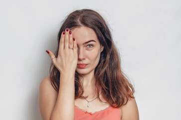 Obraz premium Cute woman with black hair covers her eye with her hand. Face close-up.