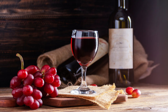 Red wine in a glass against a rustic background Alcohol, winery concept on wooden table Old and dark wooden background with bunches of red grapes.