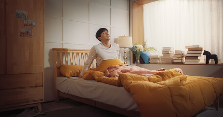Handsome Korean Young Man Wakes Up in his Bed, Sun Shines on Him, He Greets a New Sunny Day at Home and Stretches. Joyful Waking Up of an Asian Male Who is Ready for Productive Day