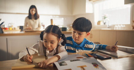 Portrait of a Korean Children Sitting at a Kitchen Table, Drawing, Writing While Mother is Preparing Breakfast. Perfect Parenting of Little Cute Kids Waiting for Nutritious Meal Before Going to School