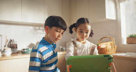 Portrait of Two Korean Kids Using a Digital Tablet During Weekend in The Kitchen. Two Cute Asian Siblings Watching Educational Content Online, Sharing the Gadget, and Enjoying Their Time