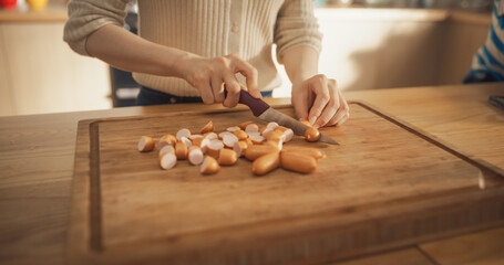 Close Up on the Hands of a Beautiful Woman Cutting Sausages in her Kitchen at Home. Focused and Carefree Housewife Using a Knife and a Cutting board to Prepare a Delicious Meal for her Family