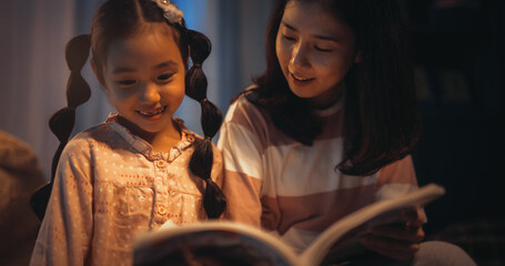 Korean Mother Reading a Fairytale to Her Lovely Small Daughter in Bed Before Going to Sleep. Young...