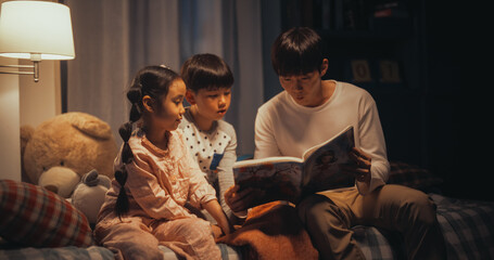 Portrait of Two Active Children Engaged in a Conversation with their Father While He Reads to them...