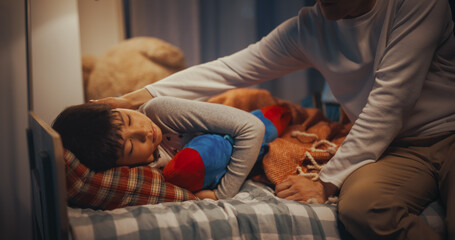 Korean Young Father Caring for His Cute Son, Putting Him to Sleep in Bed at Home in the Evening. Male Parent Tucking Little Boy in Blanket, Making Sure He is Warm and Comfortable at Night - obrazy, fototapety, plakaty