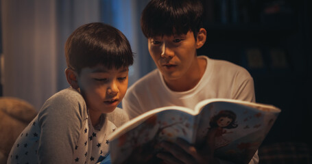 Korean Father Reading a Fairytale to His Lovely Cute Son in Bed Before Going to Sleep. Young...