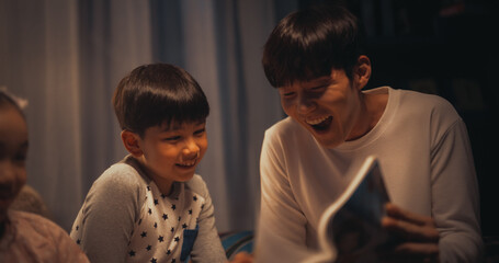 Korean Father Reading a Fairytale to His Lovely Cute Kids in Bed Before Going to Sleep. Patient...